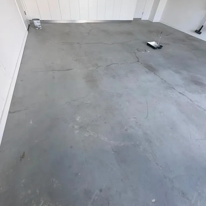 Bare grey concrete garage floor, stained and cracked, in front of white storage cabinets.
