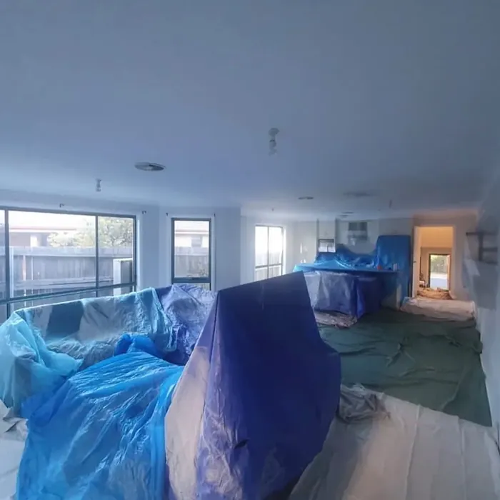 Open plan living room fully protected: furniture under plastic sheeting and drop sheets across the floor.
