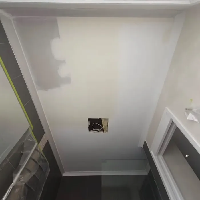 Ensuite ceiling during works: masking tape, protective sheeting and filled patches around the light cut-out.