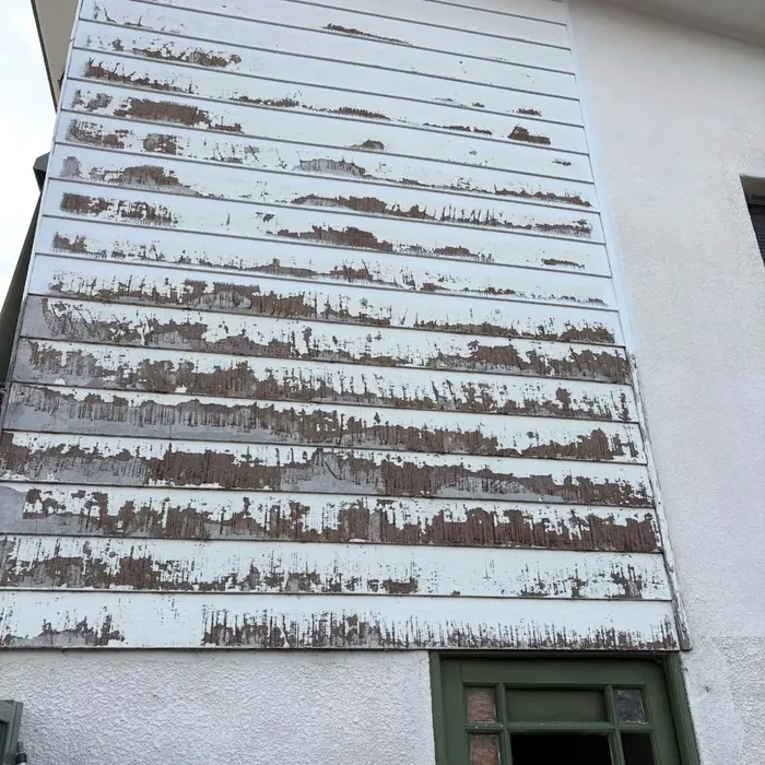 Gable-end weatherboard cladding with paint peeling and flaking across every board.
