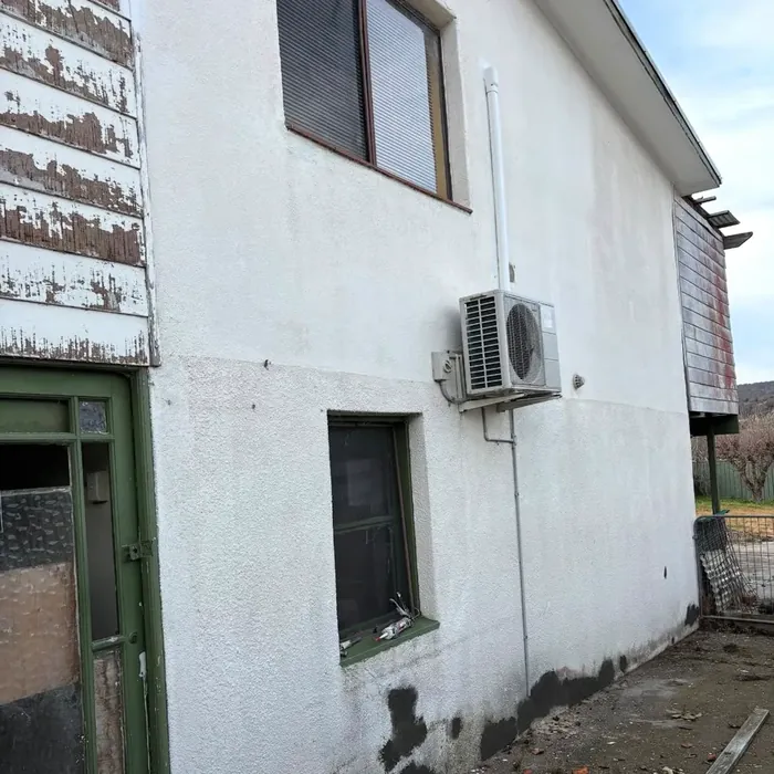 Rendered rear wall with peeling paint, water staining and a wall-mounted air conditioning unit.