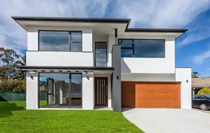 Two-storey new home exterior painted white, with timber garage door and cladding accents, Kaleen.