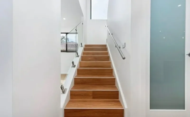 Timber staircase with crisp white walls and a glass balustrade in a newly painted home.