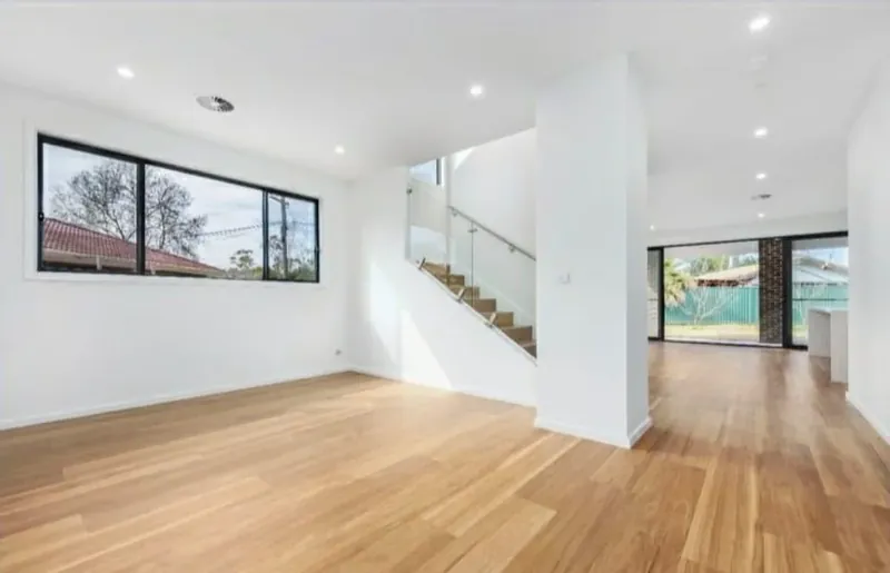 Living and dining area with white walls, timber flooring and a staircase in the background.