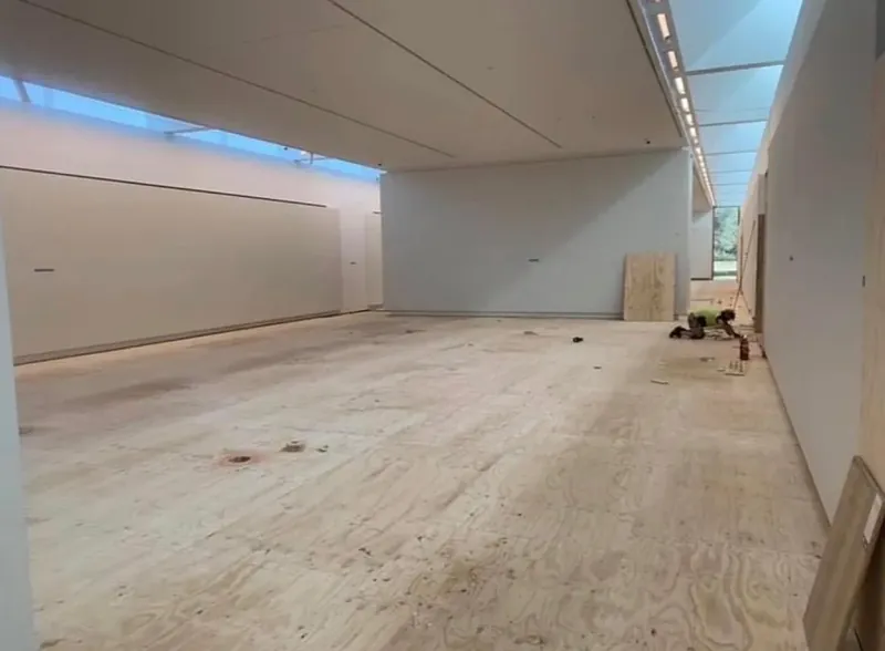 Wide gallery hall with freshly painted white walls, protective covering across the timber floor.
