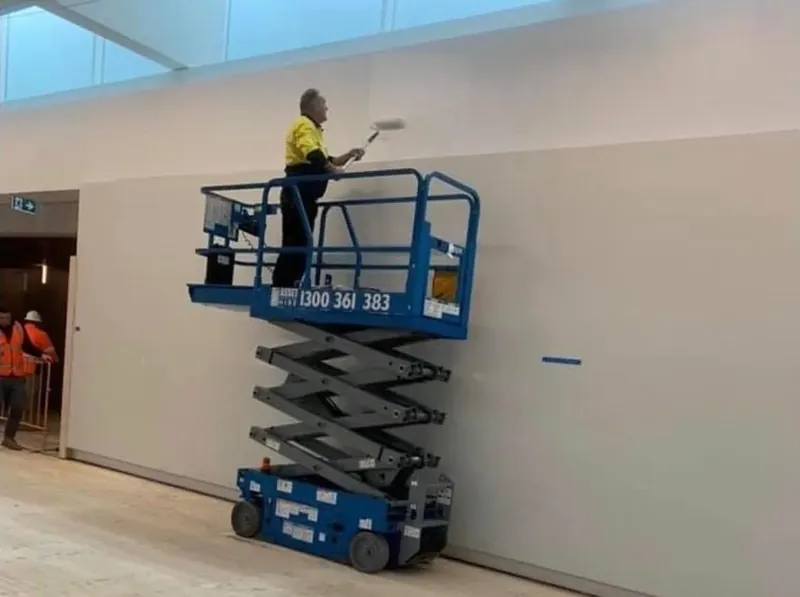 Painter working at height from a scissor lift against a tall gallery wall.