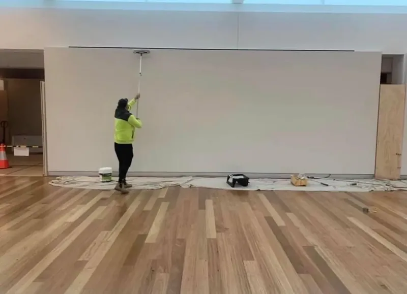 Painter in high-visibility clothing rolling a gallery wall, drop sheets across the floor.