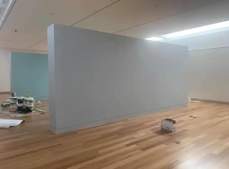 Freestanding gallery partition part-way through repainting, workspace protected.