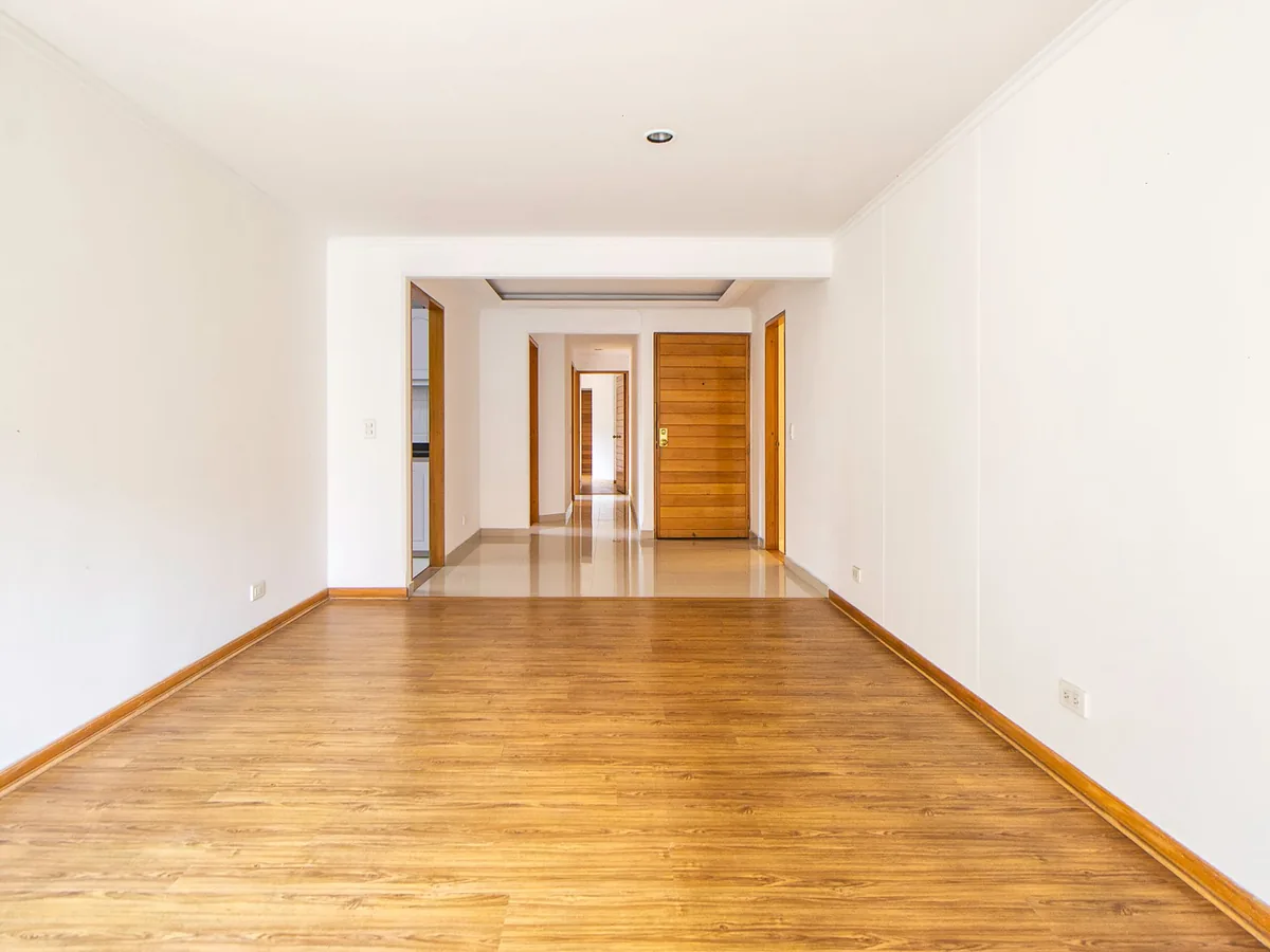 Long living space with white walls, white trim and a honey timber floor.
